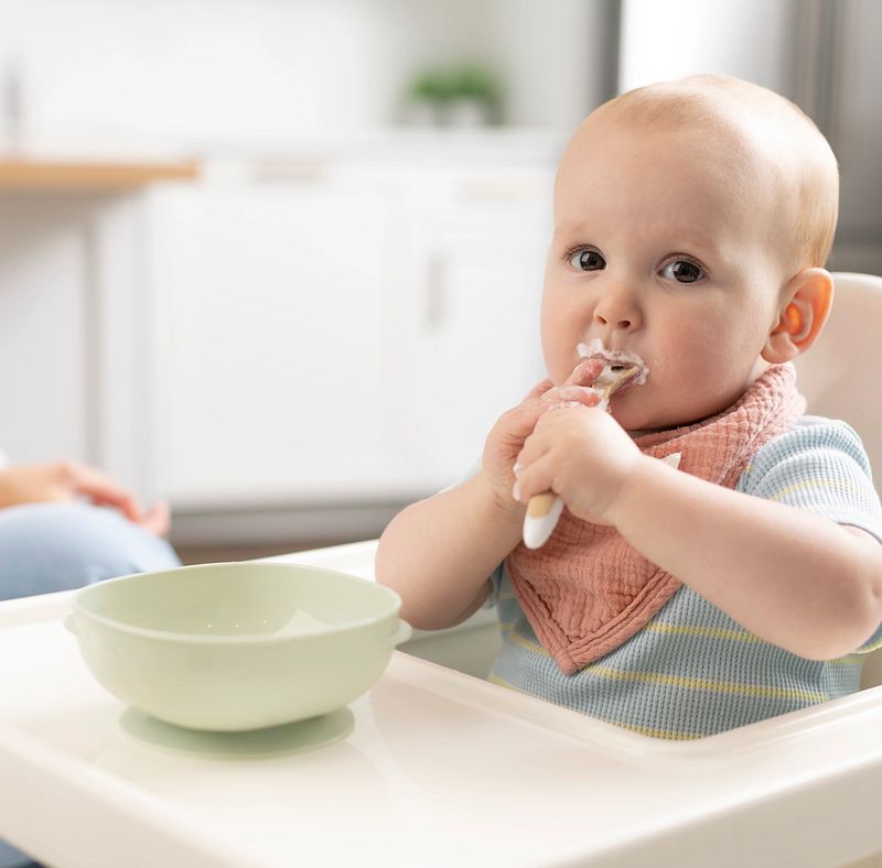 Bébé assis dans une chaise haute mangeant avec un bol à ventouse Dr. Brown’s posé sur la tablette.