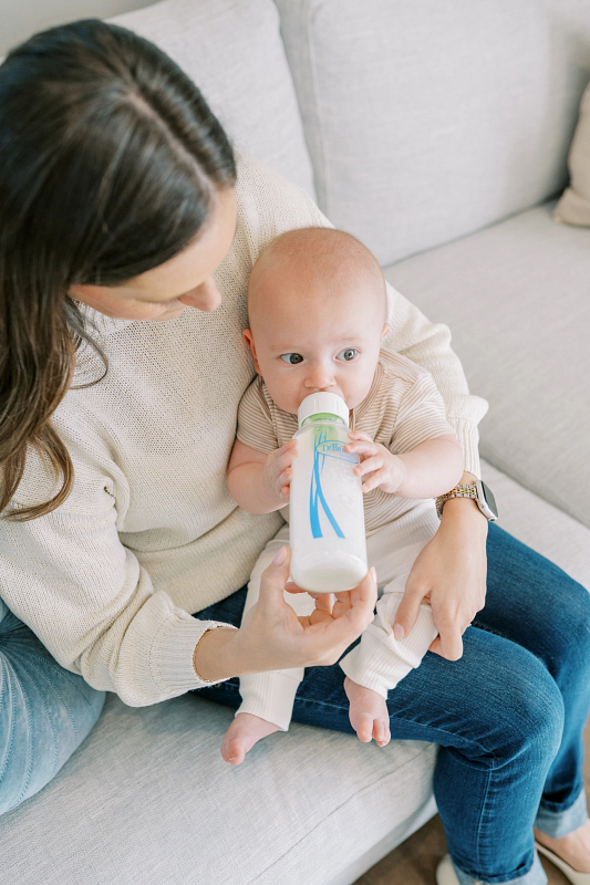 Bébé buvant au biberon en verre Dr. Brown’s dans les bras de sa maman.